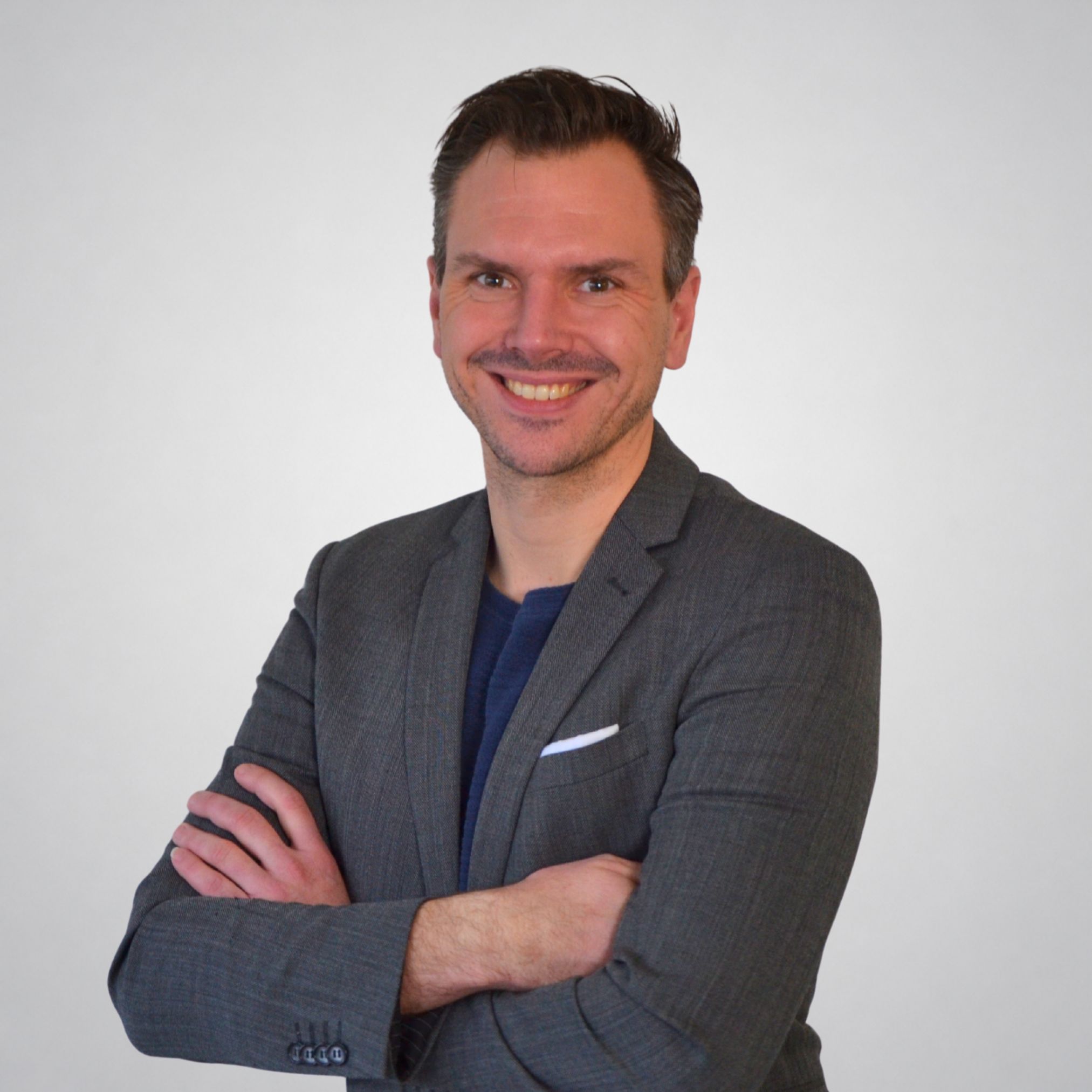 Ein Mann in einem Anzug mit verschränkten Armen lächelt.