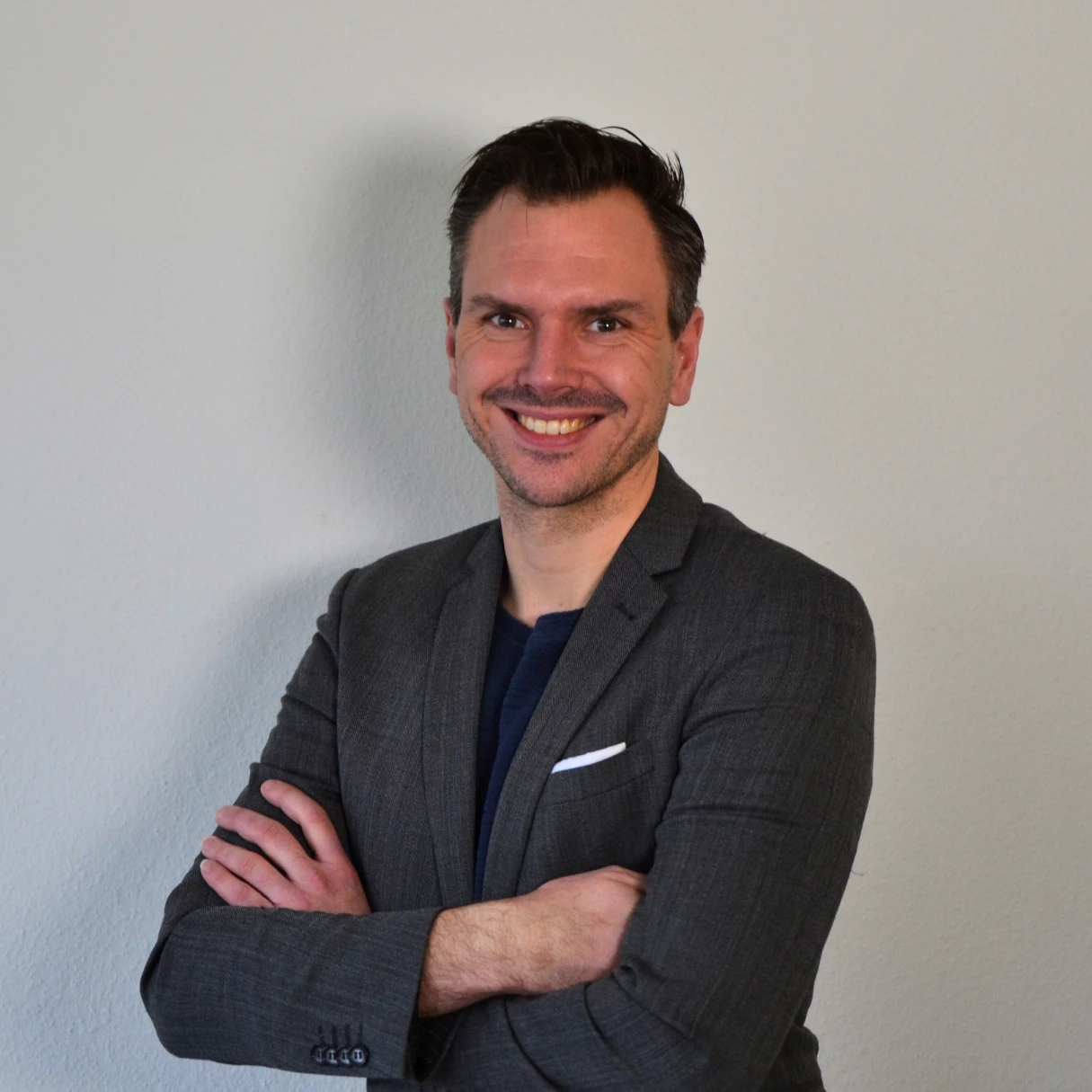 Vertrieb Ein Mann in einem Anzug mit verschränkten Armen lächelt.