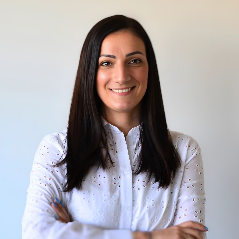 Eine lächelnde Frau mit langen Haaren in einem weißen Hemd.