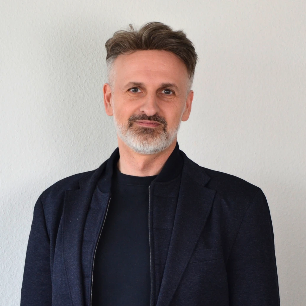 Ein Mann steht lächelnd vor einem Schild.