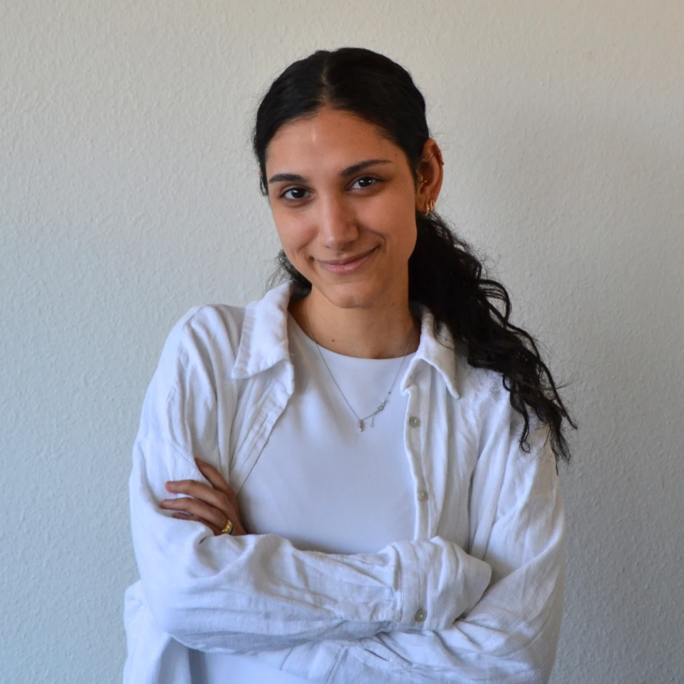 Eine lächelnde Frau mit verschränkten Armen vor einer Wand.