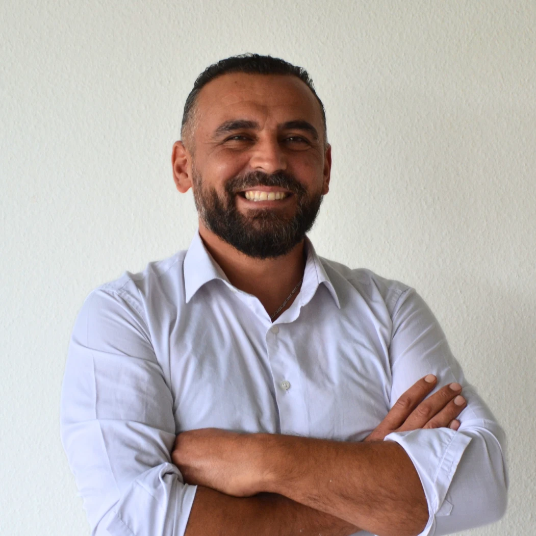 Ein Mann mit Bart und Schnurrbart trägt ein weißes Hemd und lächelt.